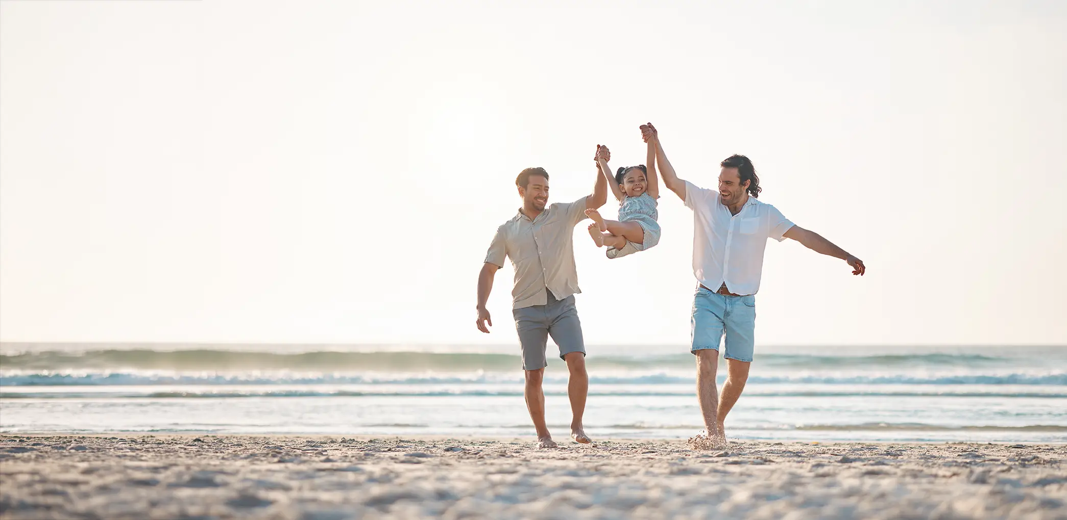 Two dads playing with their daughter at a beach Fertility Services for LGBTQ+ Parents